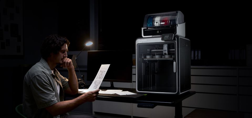 Людина працює за столом з принтером Creality K2, підкреслюючи його тиху роботу